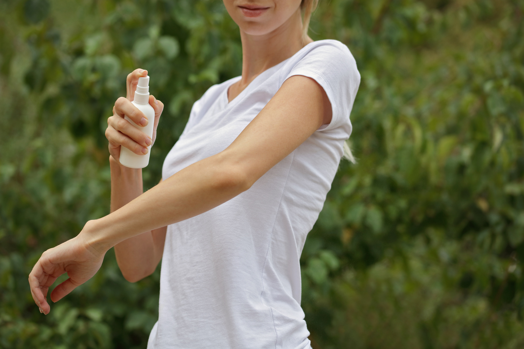 Mosquito repellent. Woman using insect repellent spray outdoors.